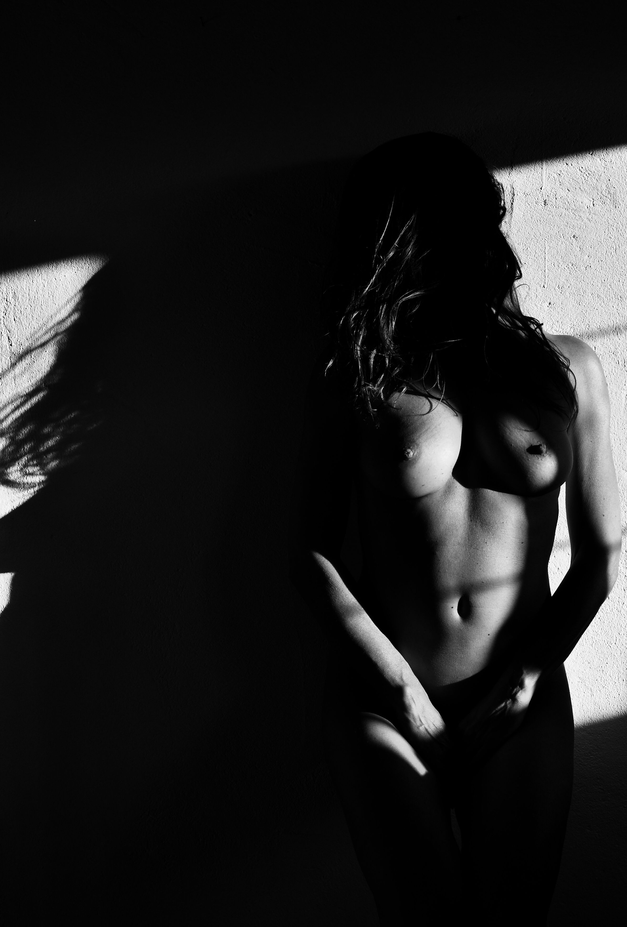 A grayscale figurative artwork showcasing a partially shadowed nude human form, embodying vulnerability and mystery through the play of light and deep chiaroscuro contrasts. Artwork style - Figurativ and technique Sublimationsdruck auf Leinwand.