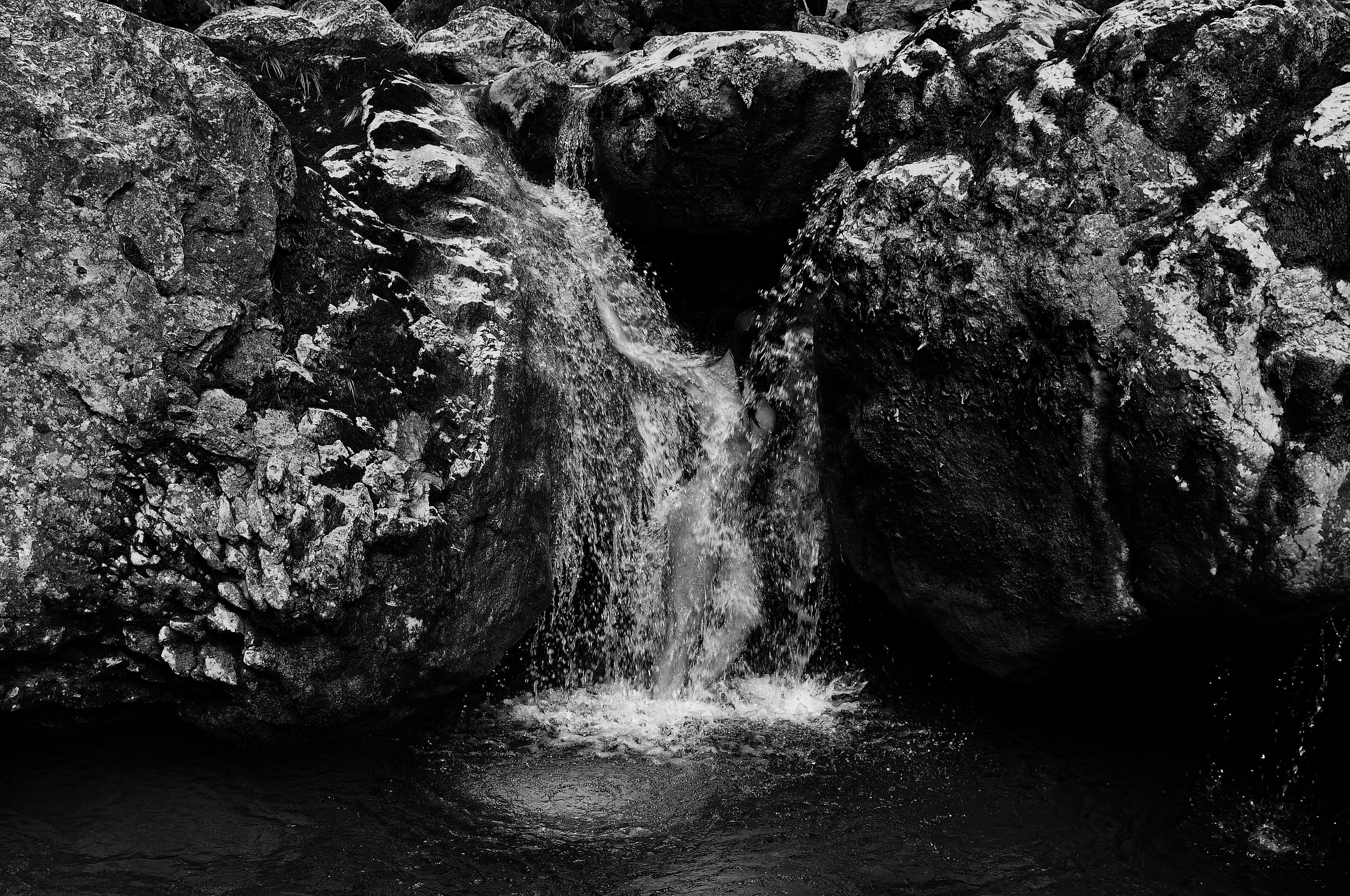 A monochrome figurative artwork on canvas captures the essence of a timeless waterfall flowing gracefully amidst rugged rocks, evoking serenity and natural motion. #Art #Nature Artwork style - Figurativ and technique Sublimationsdruck auf Leinwand.